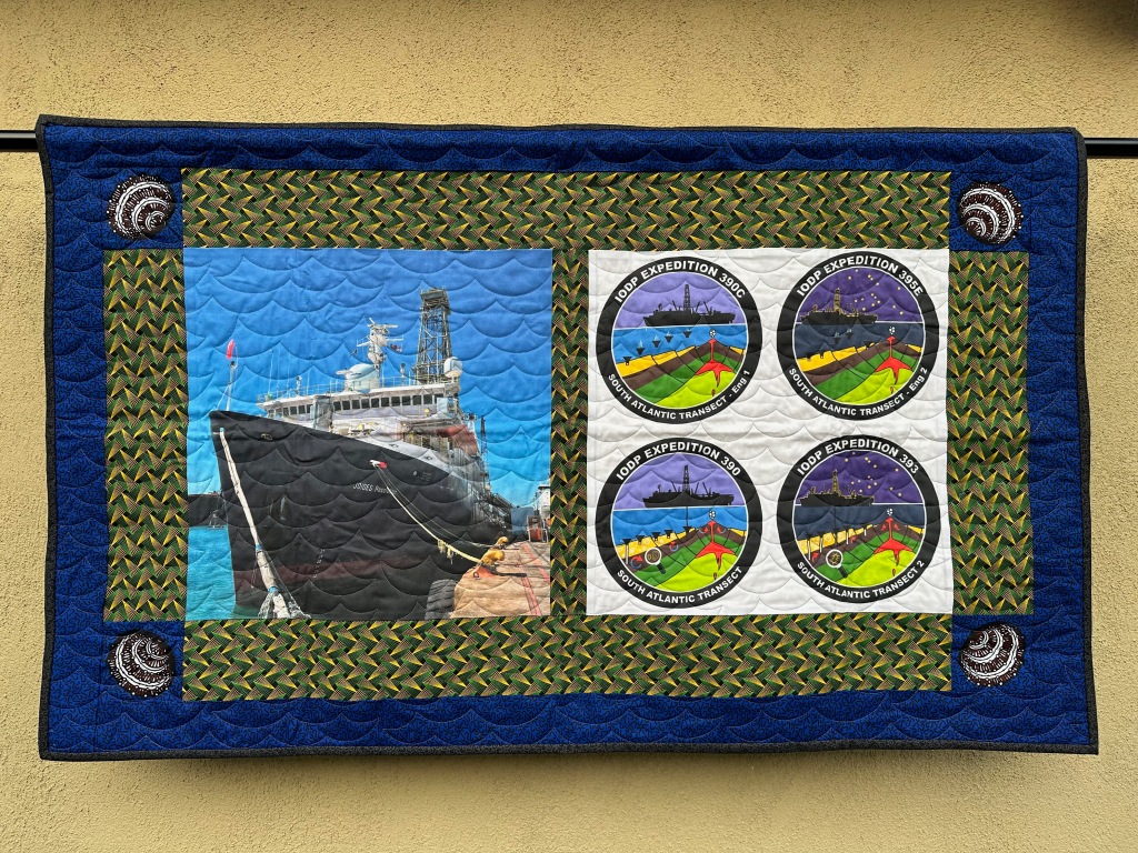 hanging quilt with a ship pictured on the left and four circle logos on the right