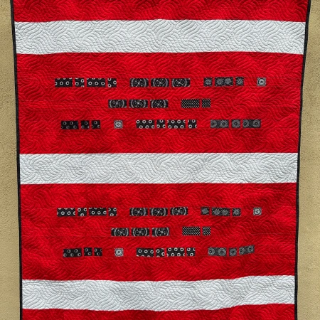 Hanging quilt with a Morse Code message in black on a red background