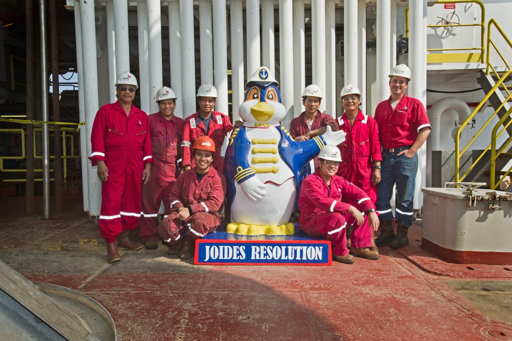 group of men wearing red coveralls posed around a penguin statue